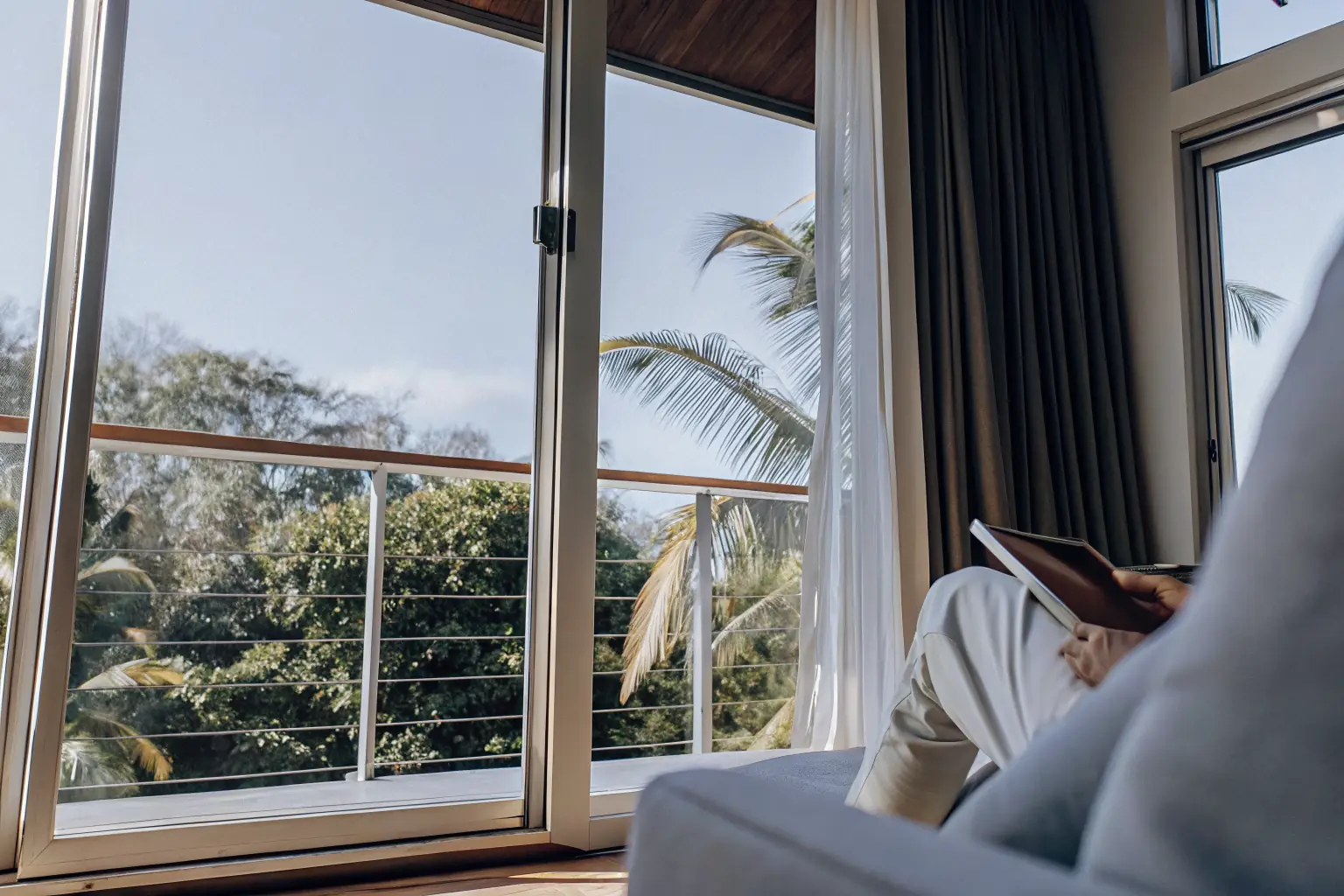 View through slider windows to a lush tropical landscape with palm trees and natural light