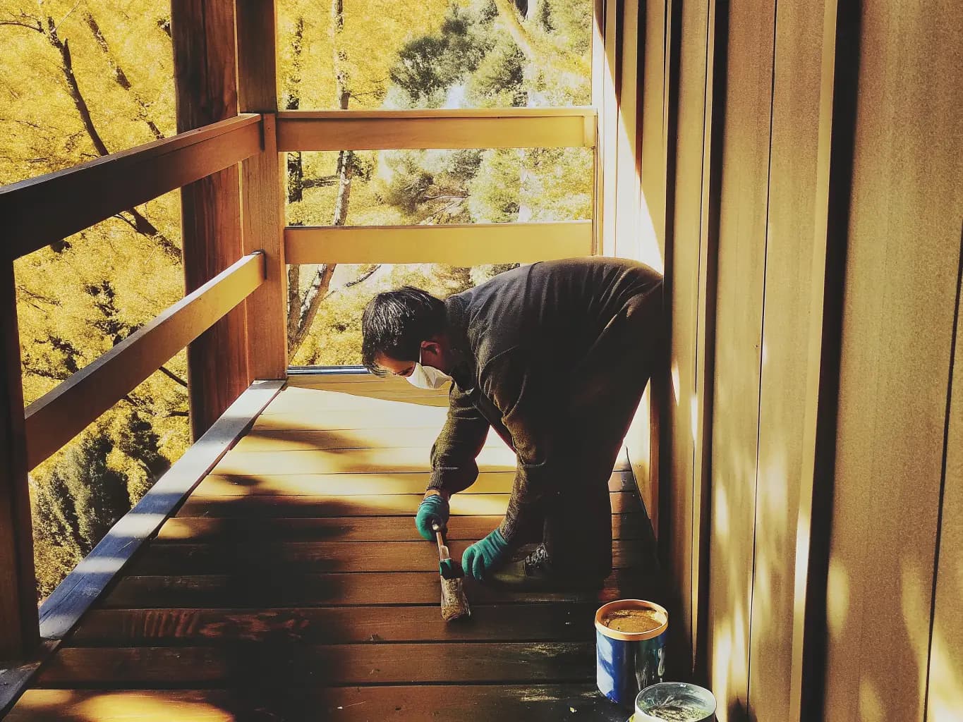 Craftsman applying natural wood stain to exterior deck with golden afternoon light